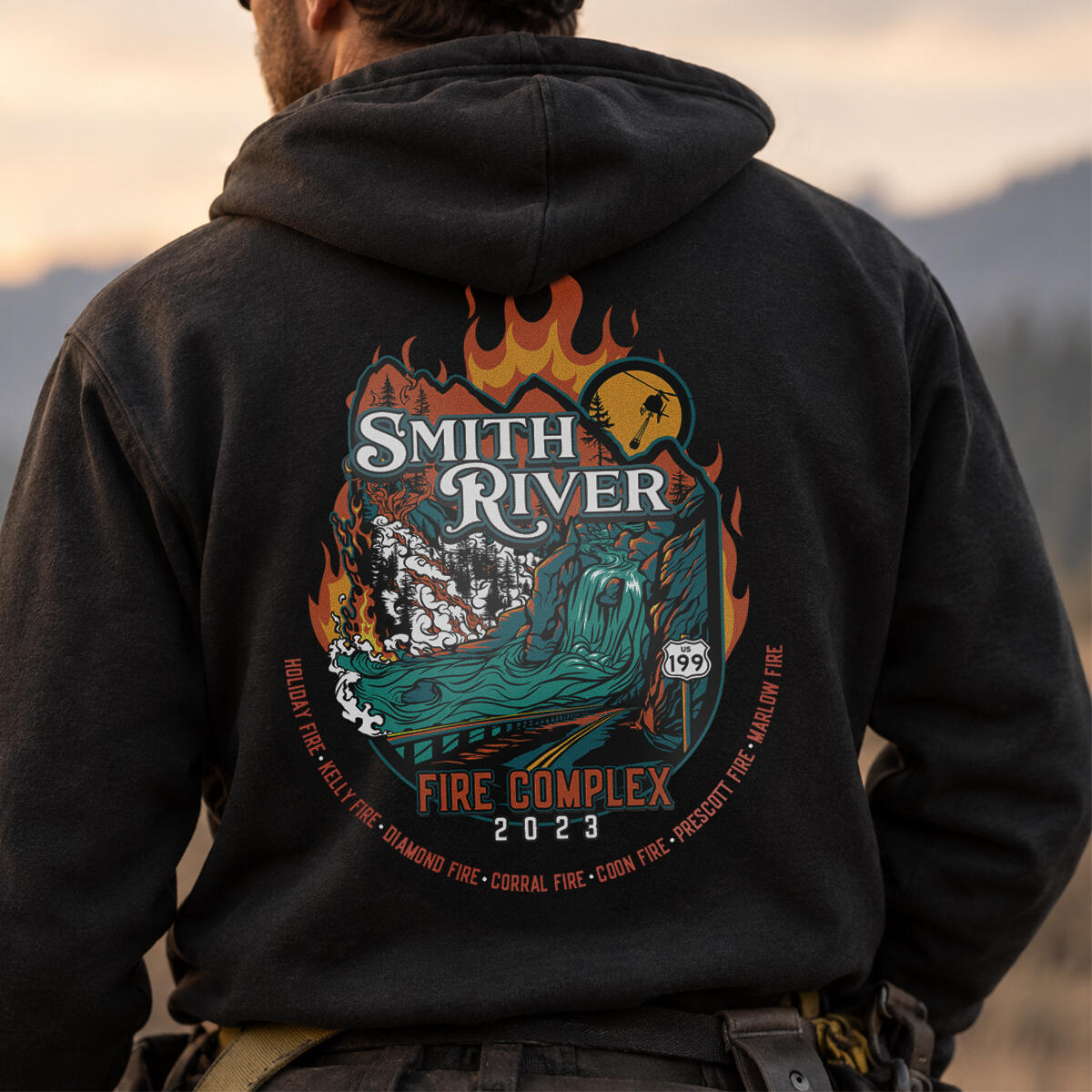 Smith River Fire Complex - Apparel Design & Illustration Black hoodie featuring a custom Smith River Fire Complex 2023 illustration with flames, forest, river, mountain scenery, and the Highway 199 shield.
