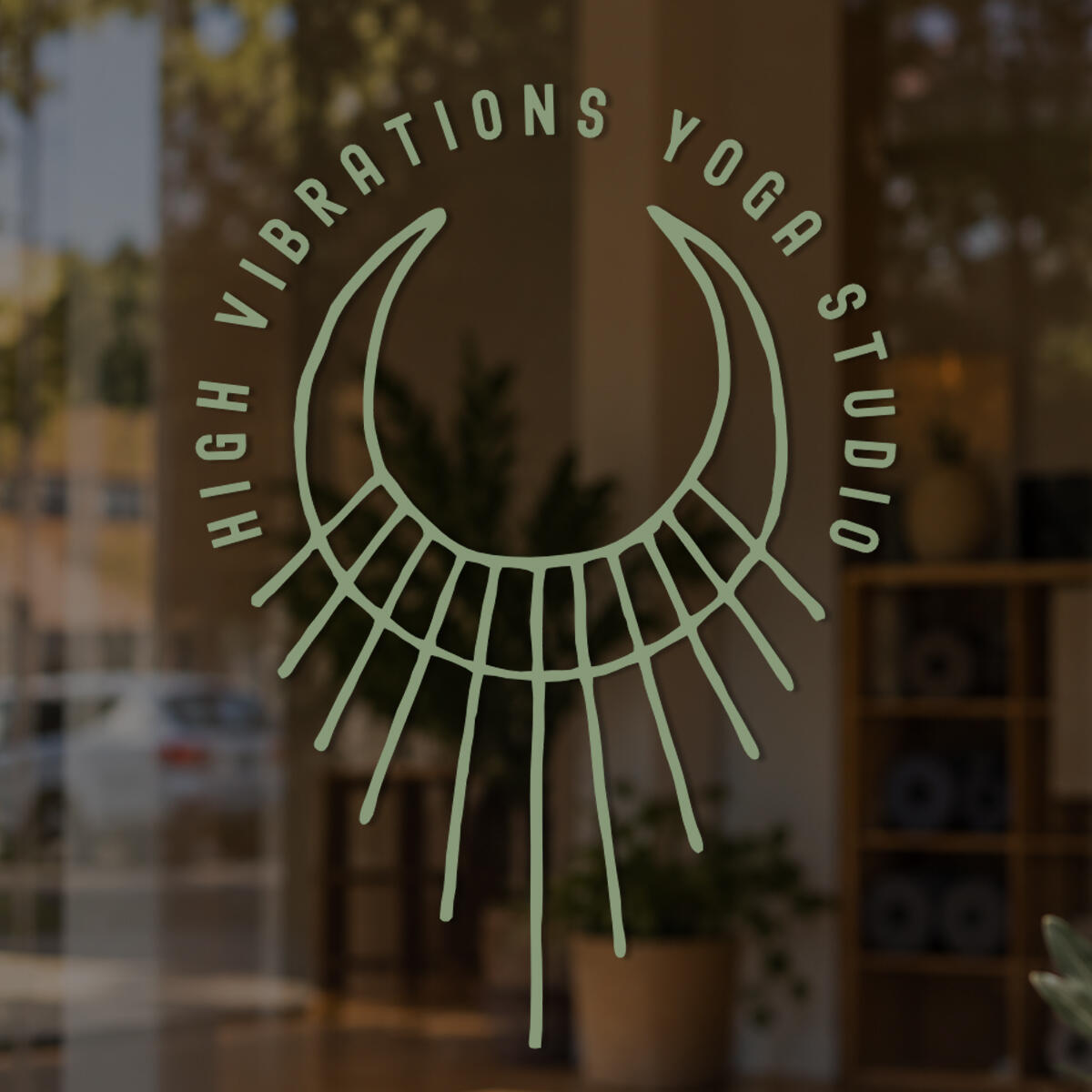 High Vibrations Yoga Studio logo applied to a storefront window, featuring a minimalist crescent-shaped symbol with radiating lines in a light green color.
